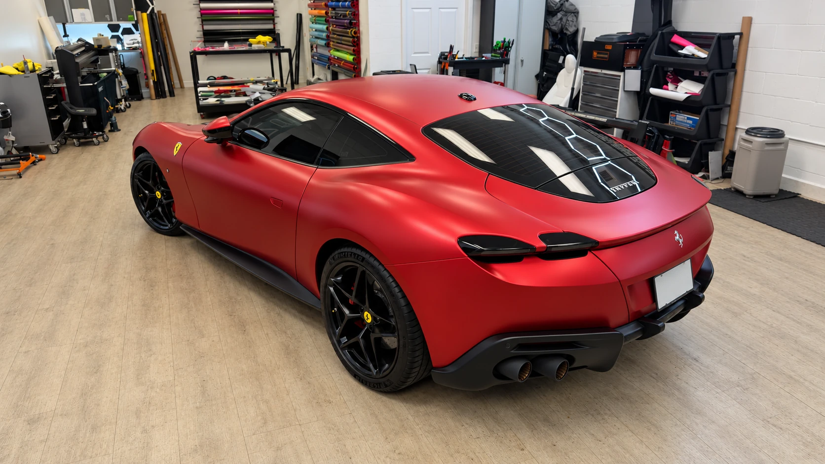 Rear three-quarter view of a matte red PPF Ferrari Roma with black wheels and dark rear trim in the Signature Customs workshop.